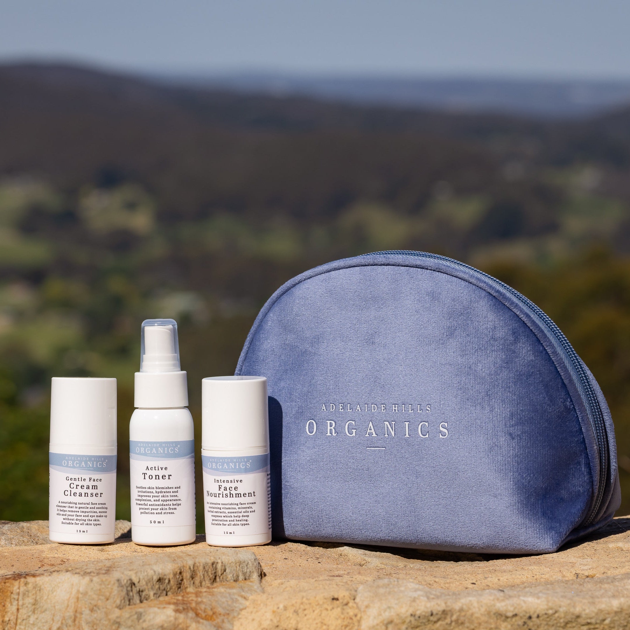 Set of skincare products and a blue pouch on a rock with a scenic background
